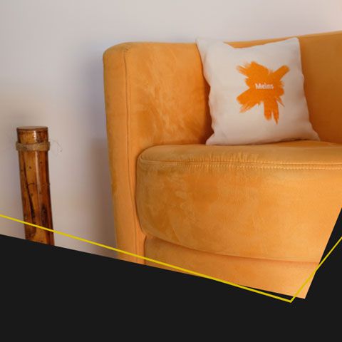 Orangefarbener Sessel mit weißem Kissen mit orangem Motiv, daneben Bambusdekoröhre