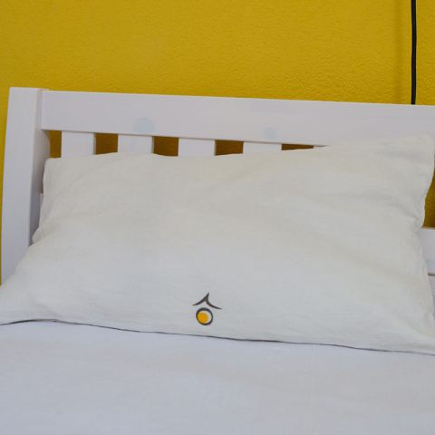 Zu sehen ist ein weißen Leinenkissen, das auf einem Bettausschnitt platziert ist. Diese Seite ist unten in der Mitte mit dem heimgold-Logozeichen bedruckt.